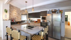 Una cocina moderna con una isla central, electrodomésticos de acero inoxidable y sillas de mimbre.