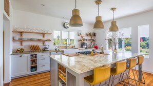 Una cucina moderna con isola centrale, sgabelli da bar, mensole in legno e un'ampia finestra vista su piante.
