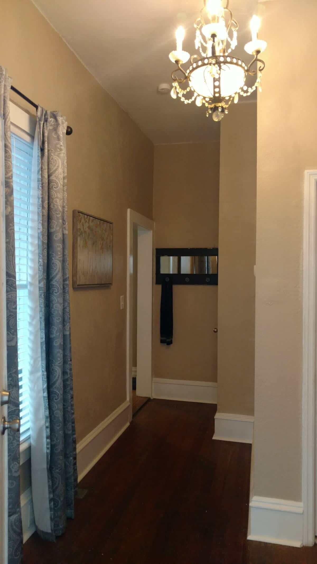 A hallway with a chandelier, patterned curtains, and a mirror on the wall.