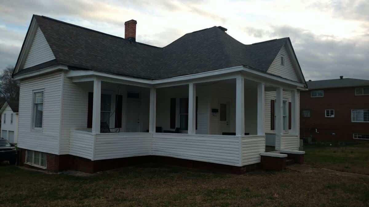 A two-story house with a wrap-around porch, a chimney, and a brick foundation.