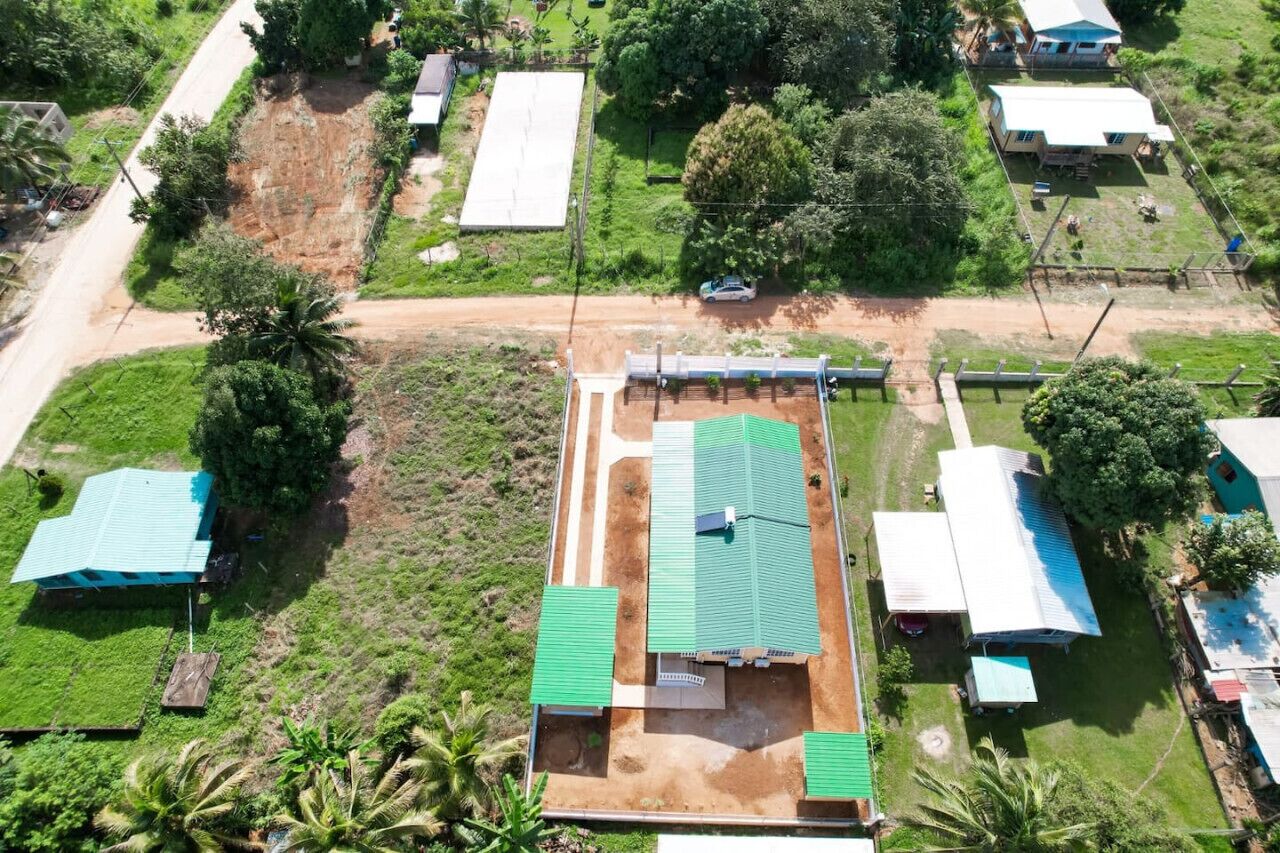 An aerial view of a residential area with multiple houses, a dirt road, and green vegetation.