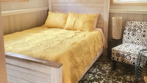 A bedroom with a wooden bed, yellow bedding, a decorative wall piece, and a patterned chair.