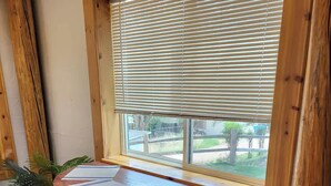 A corner room with a wooden table and bench, a window with blinds, and a potted plant.