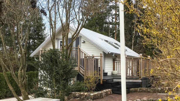 A two-story house with a porch, surrounded by trees and a stone wall. - 2 bedroom gorgeous home in åkersberga (Åkersberga)