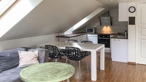 A compact kitchen with white cabinets, a microwave, and a stove. There is a dining area with a white table and black chairs. A green ottoman is visible. - 2 bedroom gorgeous home in åkersberga (Åkersberga)
