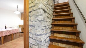 A wooden staircase with a stone wall, a dining area with a table and chairs, and a hanging light fixture. - Awesome home in Loazzolo with WiFi (Loazzolo)