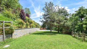 A grassy backyard with a stone wall, a wooden fence, and a wooden structure in the background. - Awesome home in Loazzolo with WiFi (Loazzolo)