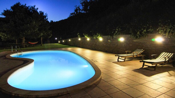 A swimming pool with a curved edge, surrounded by a tiled deck. There are two lounge chairs and a hammock. - Awesome home in Loazzolo with WiFi (Loazzolo)