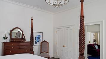 Un dormitorio con cama con dosel, cómoda, espejo, una obra de arte enmarcada y una puerta que da a otra habitación.