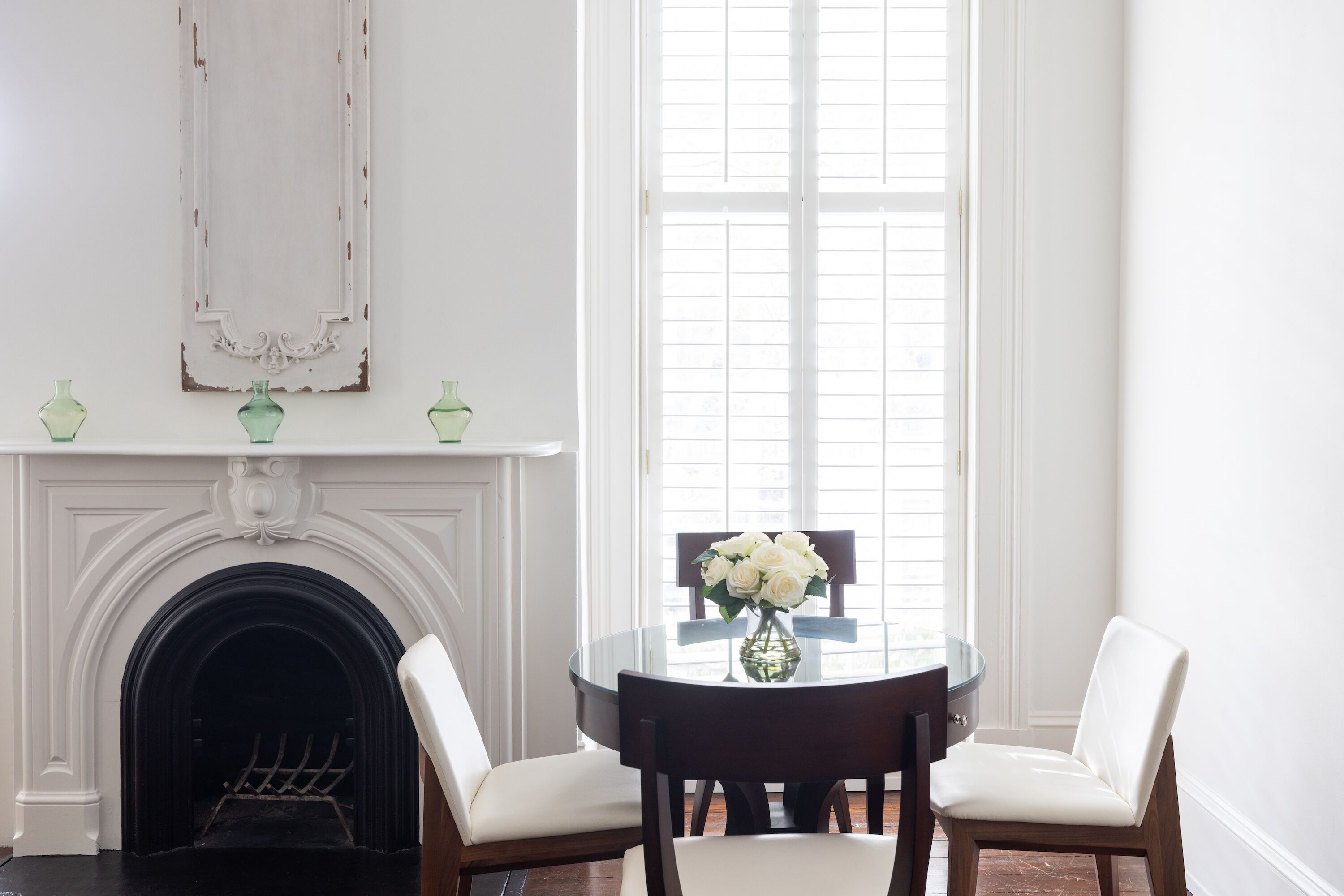 A room with a fireplace, a round table with chairs, and a window with blinds.