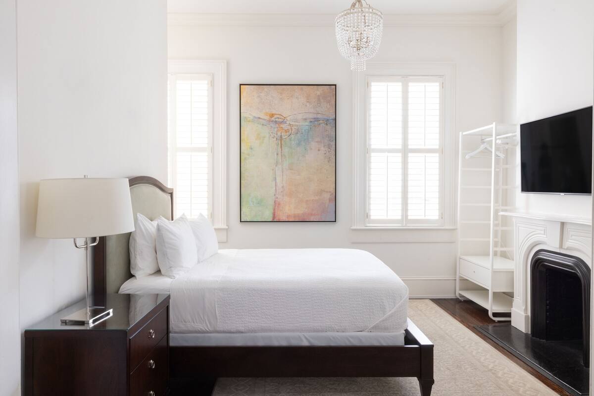 Quarto com cama, mesa de cabeceira, abajur, quadro, televisão e lareira.