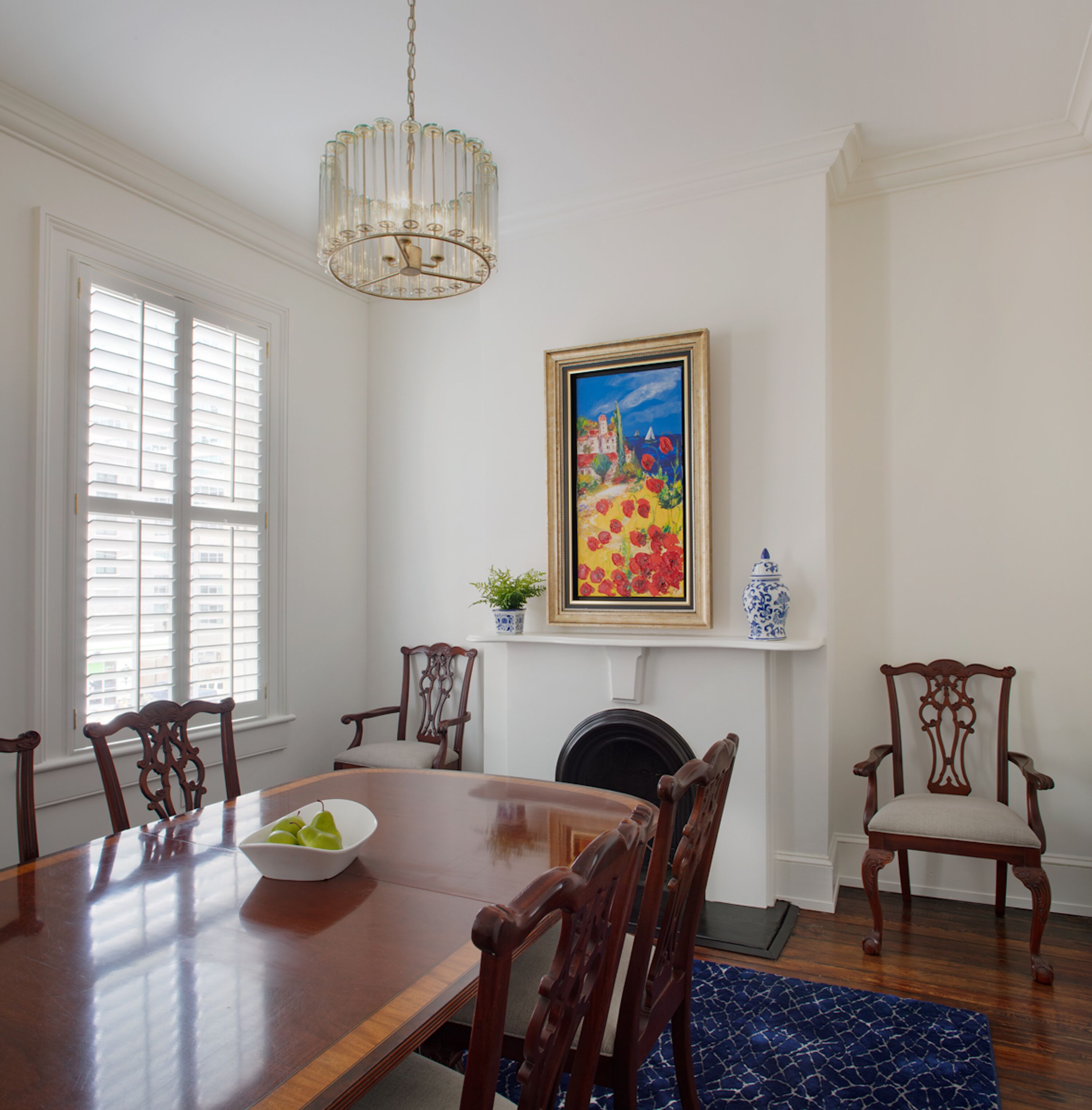 A dining room with a wooden table, chairs, a chandelier, a fireplace, and a painting.