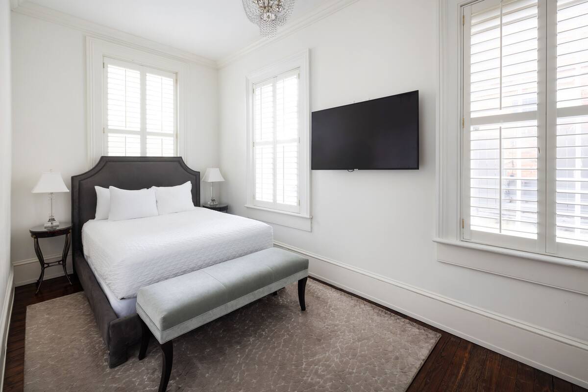 Quarto com cama grande, duas mesas de cabeceira, um banco e uma TV de tela plana na parede.