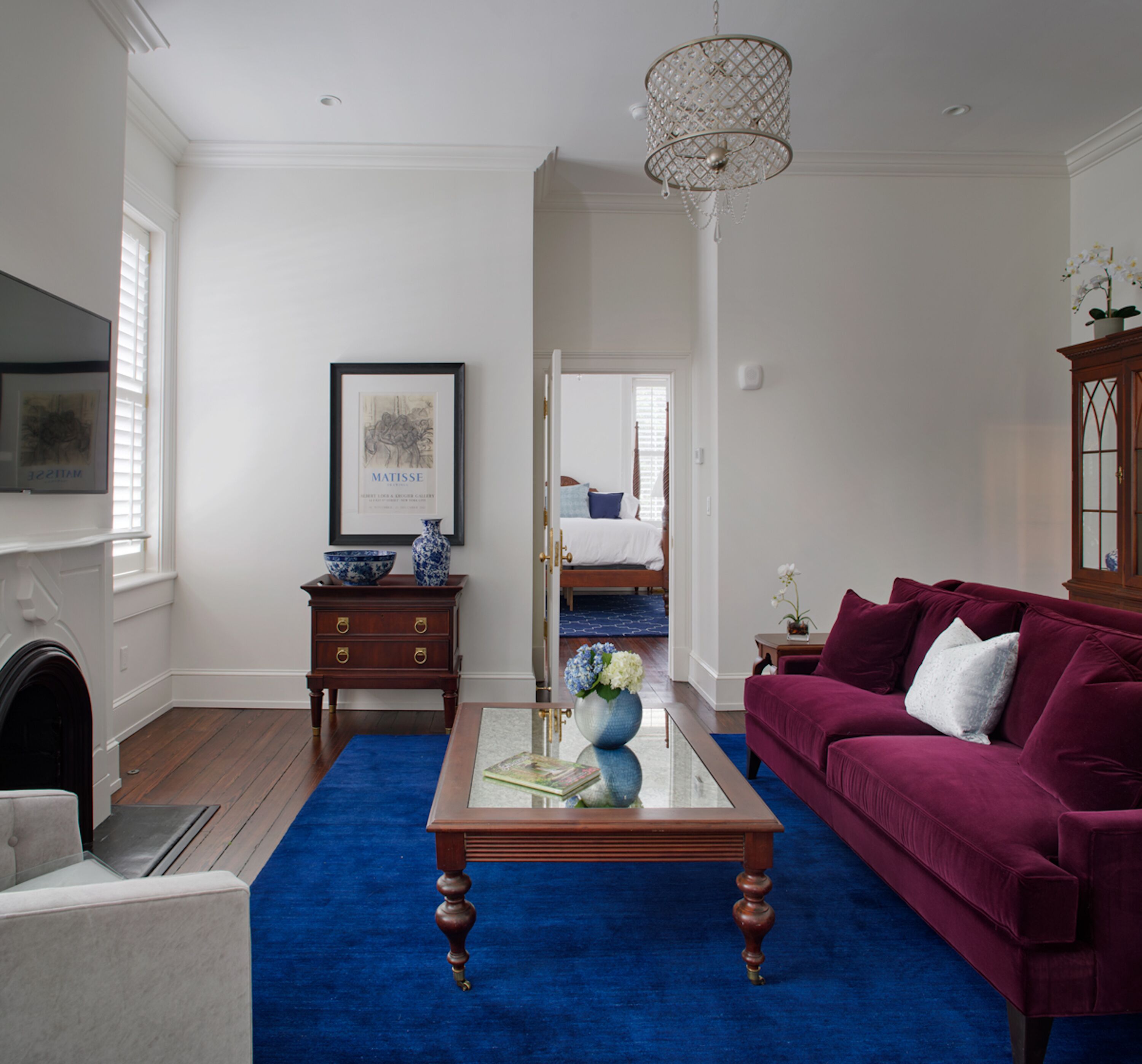 A living room with a blue carpet, a red sofa, a wooden coffee table, and a chandelier.