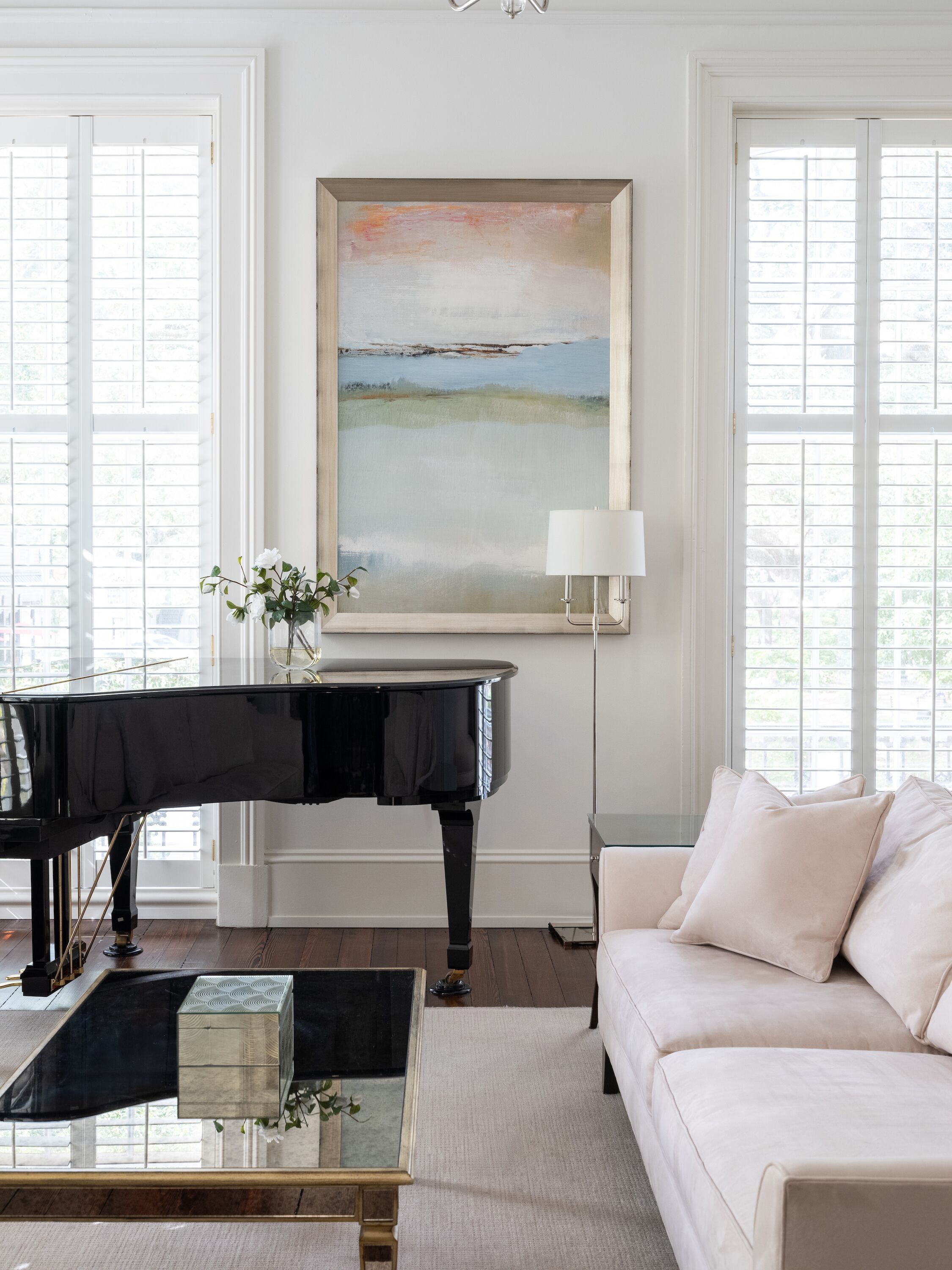 A living room with a grand piano, a sofa, a coffee table, and a painting on the wall.