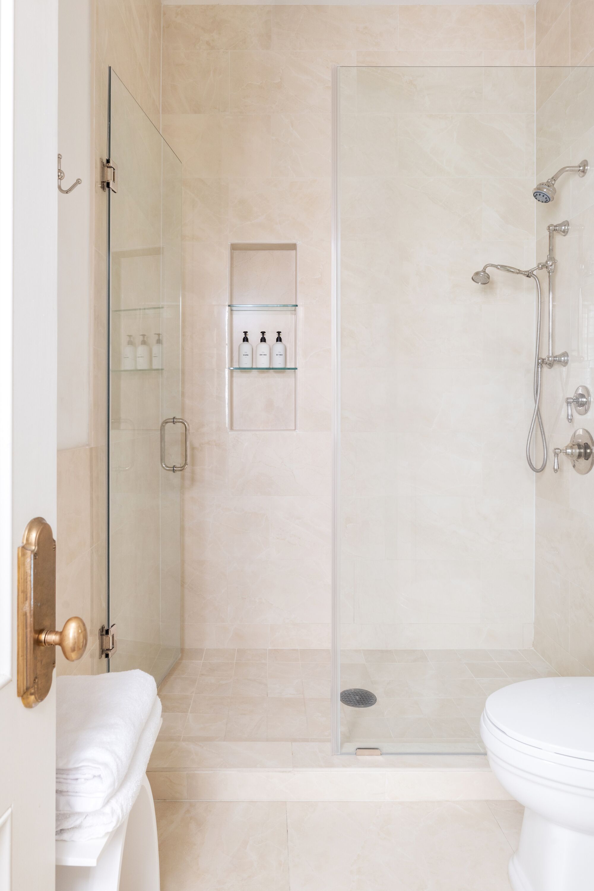 A modern bathroom with a glass-enclosed shower, a toilet, and a glass shelf with toiletries.