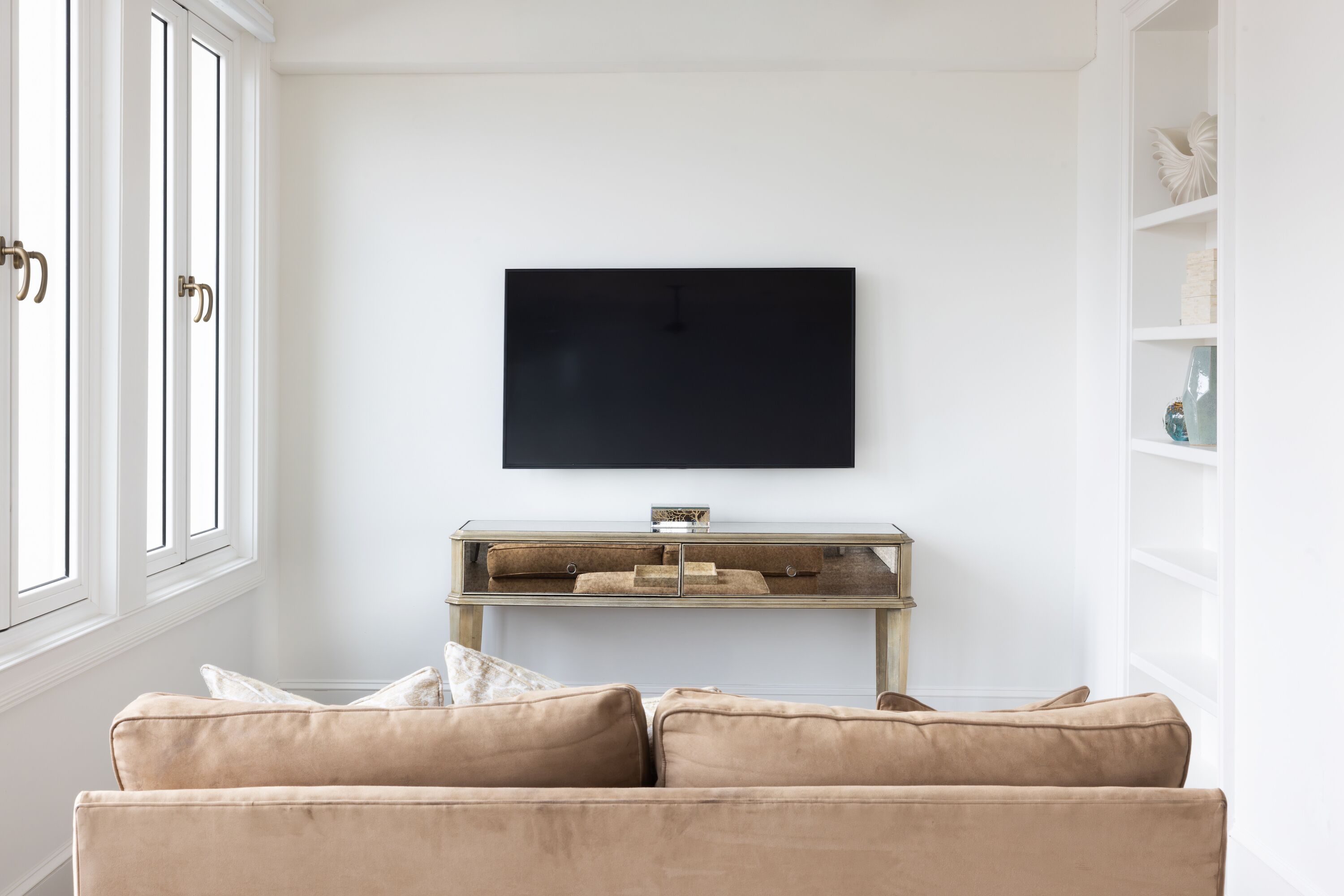 Una sala de estar con un sofá color crema, un televisor montado en la pared y un mueble bajo de madera.