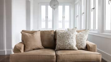 A beige sectional sofa with patterned cushions in a bright, white-walled room with large windows and a hanging light fixture.
