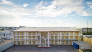 Un motel de varios pisos con una escalera central, un estacionamiento y un cielo despejado.