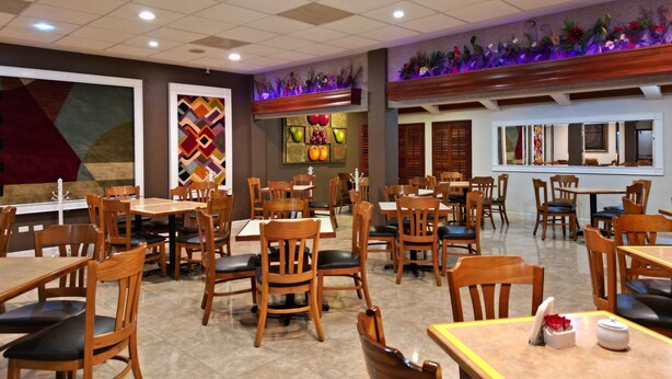 Un restaurante con mesas y sillas de madera, piso de baldosas y una pared decorativa con pinturas de frutas.