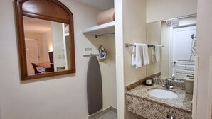 Un baño con un espejo grande, una tabla de planchar, un perchero y un lavabo con encimera de granito.