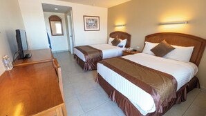 Habitación de hotel con dos camas, un escritorio, un televisor y un baño visible a través de una puerta abierta.