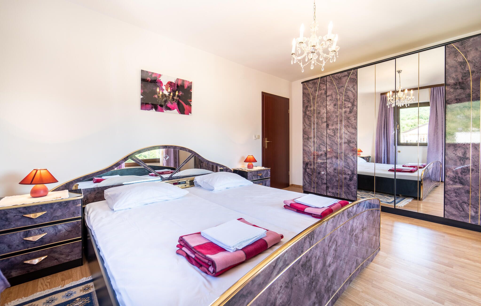 A modern bedroom with a large bed, bedside lamps, a mirror, and a chandelier.