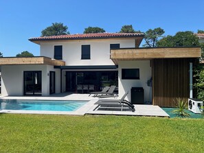 Ein modernes, zweistöckiges Haus mit Schwimmbad, Sitzgelegenheiten im Freien und einer Holzterrasse.