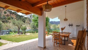 A covered patio with a wooden table and chairs, a herringbone-patterned floor, and a view of a lake and hills. - Beach front home in Solanas, Sinnai with WiFi (Solanas, Sinnai)