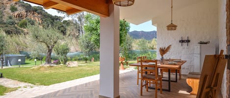 A covered patio with a wooden table and chairs, a herringbone-patterned floor, and a view of a lake and hills.