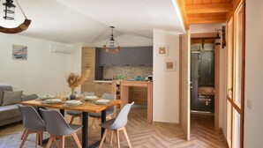 A modern kitchen with wooden cabinets, a dining area with a wooden table and chairs, and a visible bathroom with a glass door. - Beach front home in Solanas, Sinnai with WiFi (Solanas, Sinnai)