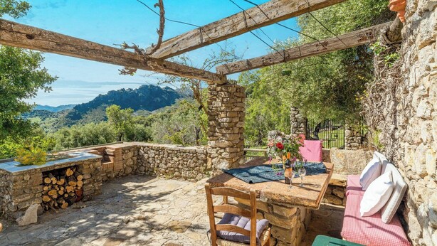 Un espace extérieur aménagé dans un style rustique, avec des murs en pierre, une table en bois et une vue sur le paysage environnant.