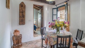 Un coin repas avec une table dressée pour deux personnes, un vase de fleurs et un tabouret en bois rustique.