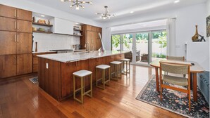 A modern kitchen with wooden cabinets, a central island with stools, and a dining area with a table and chairs.