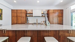A modern kitchen with wooden cabinets, a marble countertop, and bar stools.