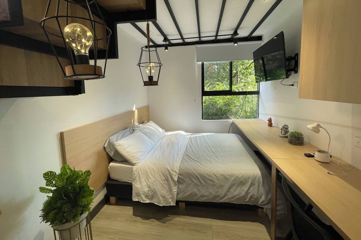 Un dormitorio pequeño con cama, mesita de noche y ventana con vistas a zonas verdes.