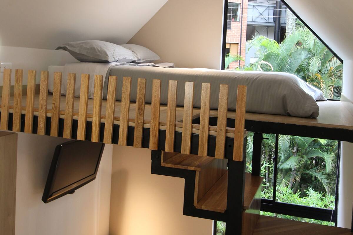 Un dormitorio tipo loft moderno con una cama litera, un escritorio y un amplio ventanal que ofrece vistas a zonas verdes.