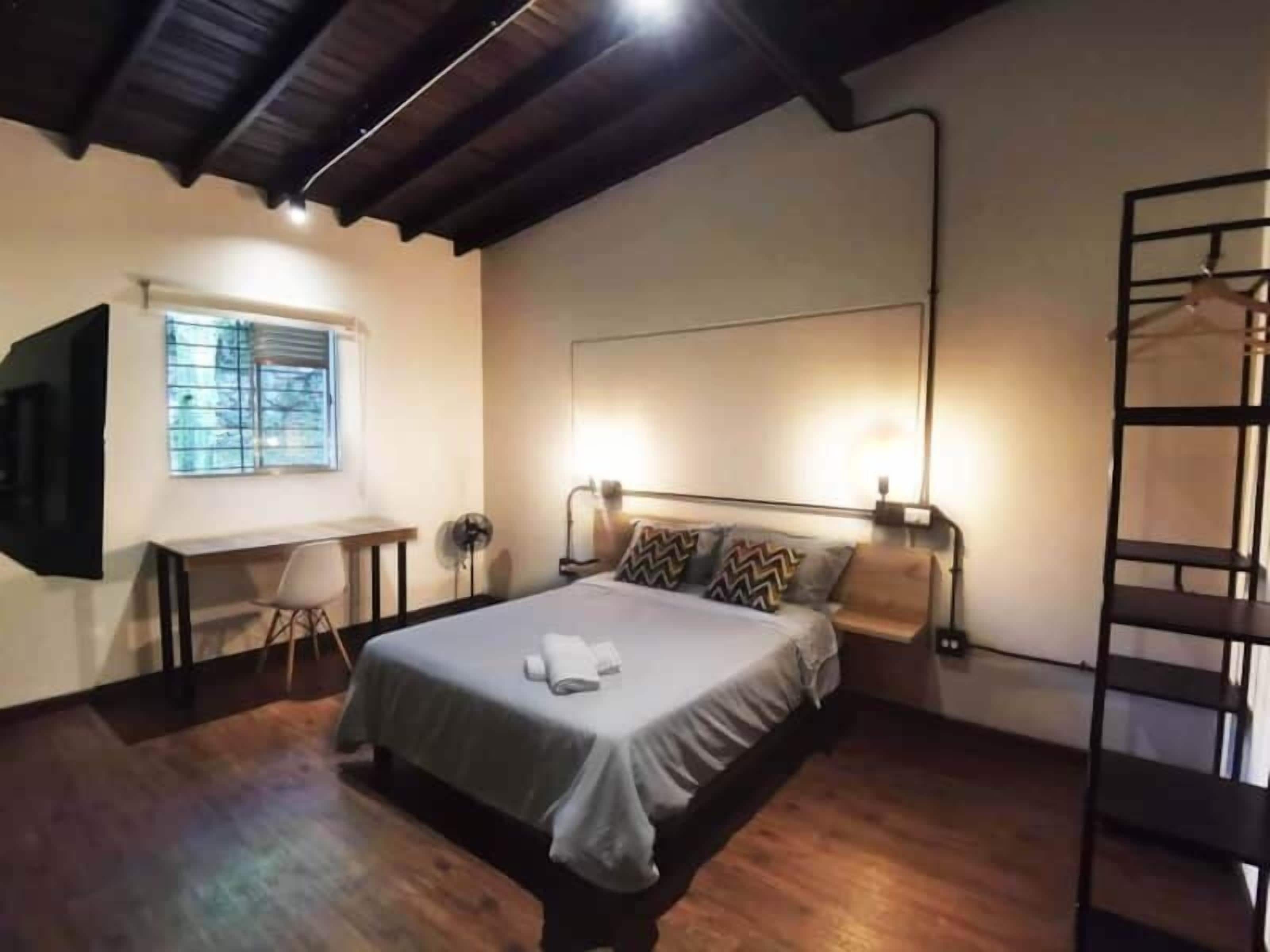 A bedroom with a bed, bedside lamps, a TV mounted on the wall, a window, and a wooden floor.