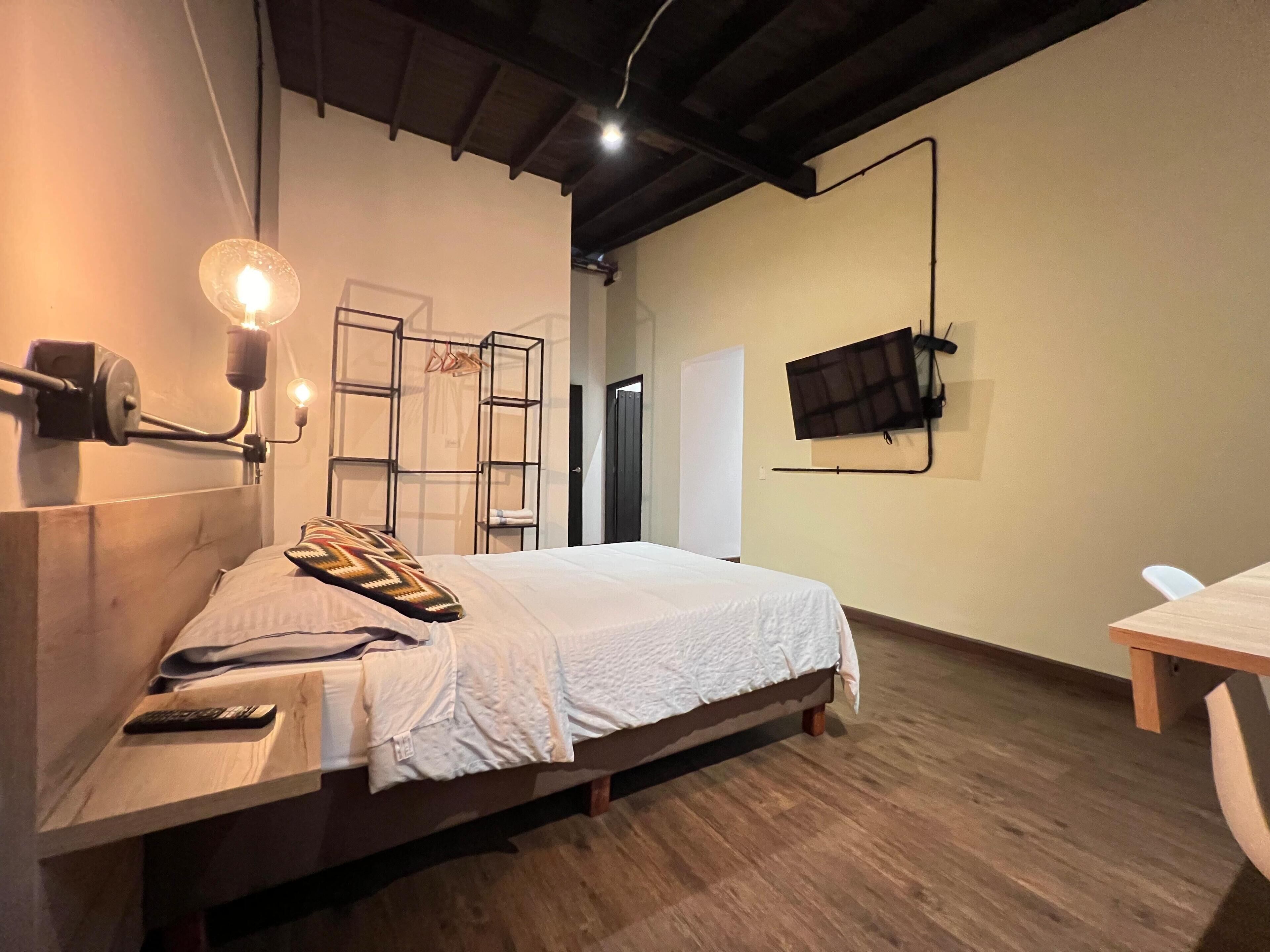 Un dormitorio con cama, mesita de noche, lámpara, armario y televisor montado en la pared.