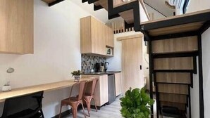 A modern kitchen with wooden cabinets, a dining area with a table and chairs, and a staircase with a metal railing. - Frontera by Roots Rentals (Medellín)