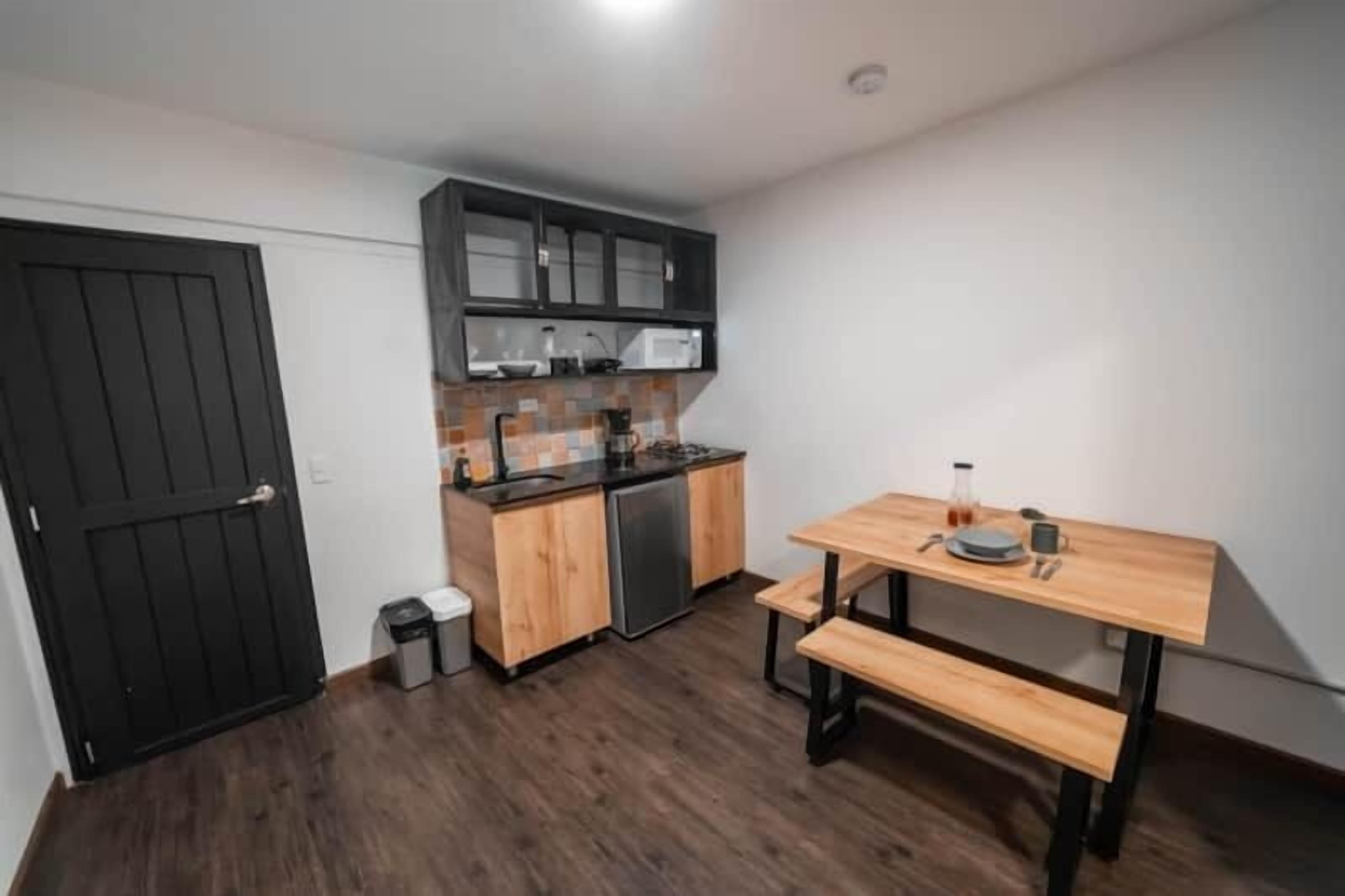 A compact kitchen with dark cabinets, a microwave, and a wooden table with benches.