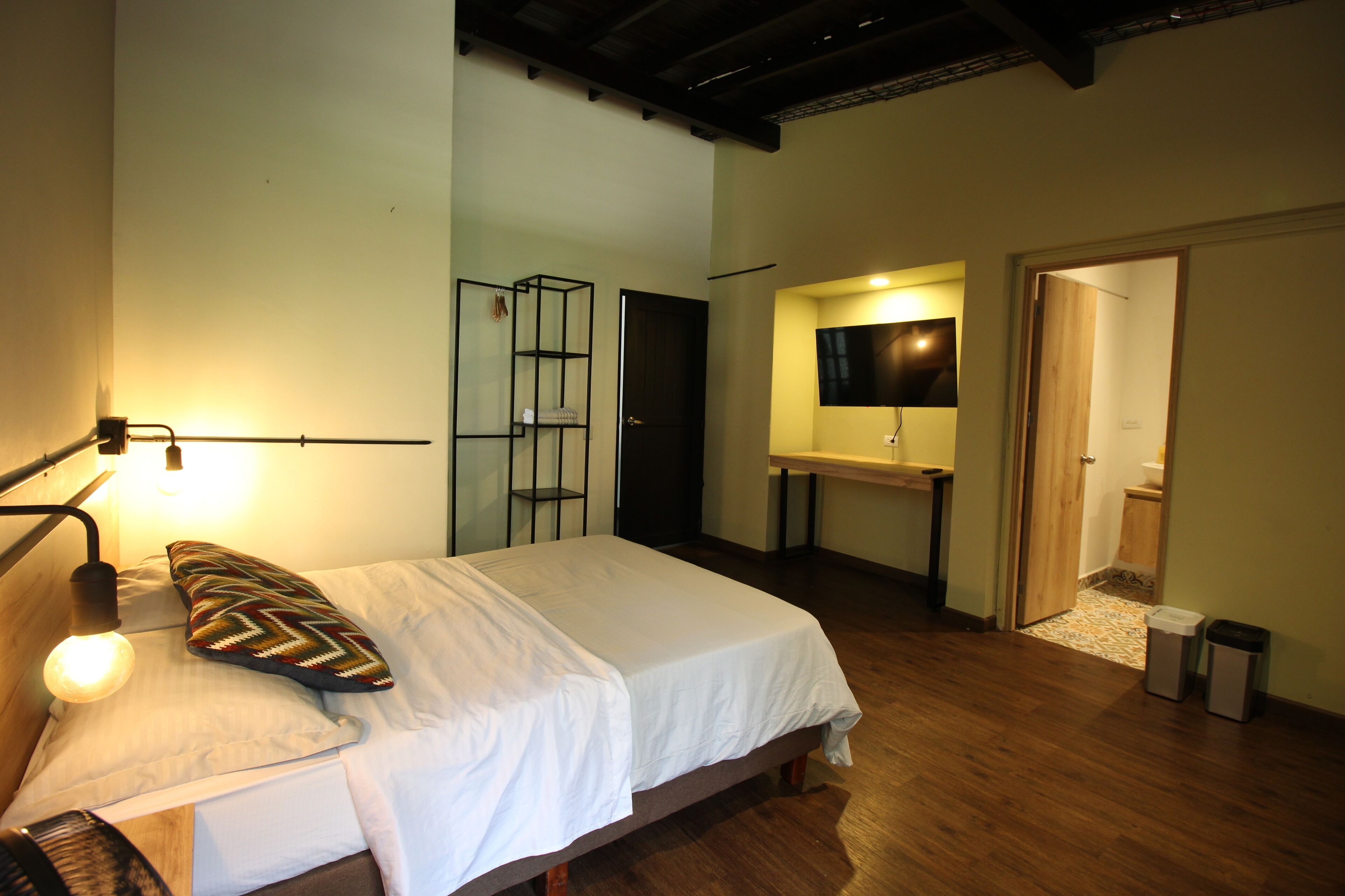 A bedroom with a bed, bedside lamp, and a mirror above a wooden dresser.