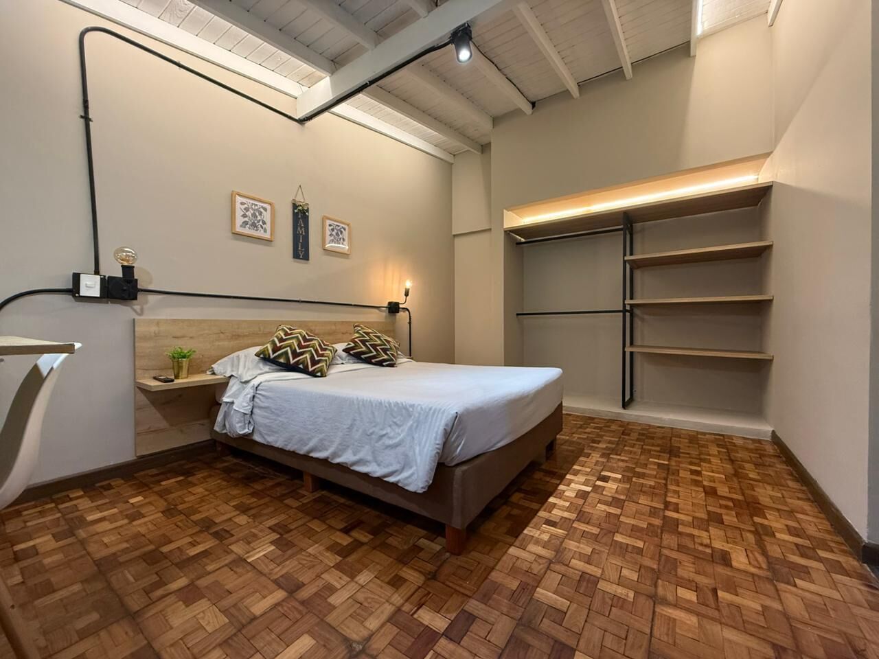 Ein Schlafzimmer mit Bett, Holzboden, einem Kopfteil, Wandregalen und einer Deckenleuchte.