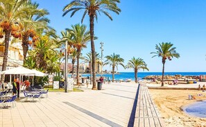 A beachside promenade with palm trees, a wooden walkway, and beach chairs.