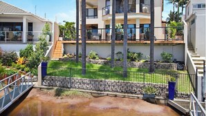 A modern two-story house with a balcony, surrounded by a well-maintained garden and palm trees. - Beautiful Family Home with Heated Pool on the Water (Bundall)
