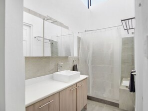 A modern bathroom with a white sink, wooden cabinets, a large mirror, and a glass shower enclosure. - Casa Bellavista (San José)