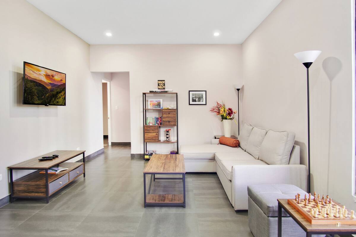 A modern living room with a sofa, a coffee table, a TV, a bookshelf, and a chessboard.