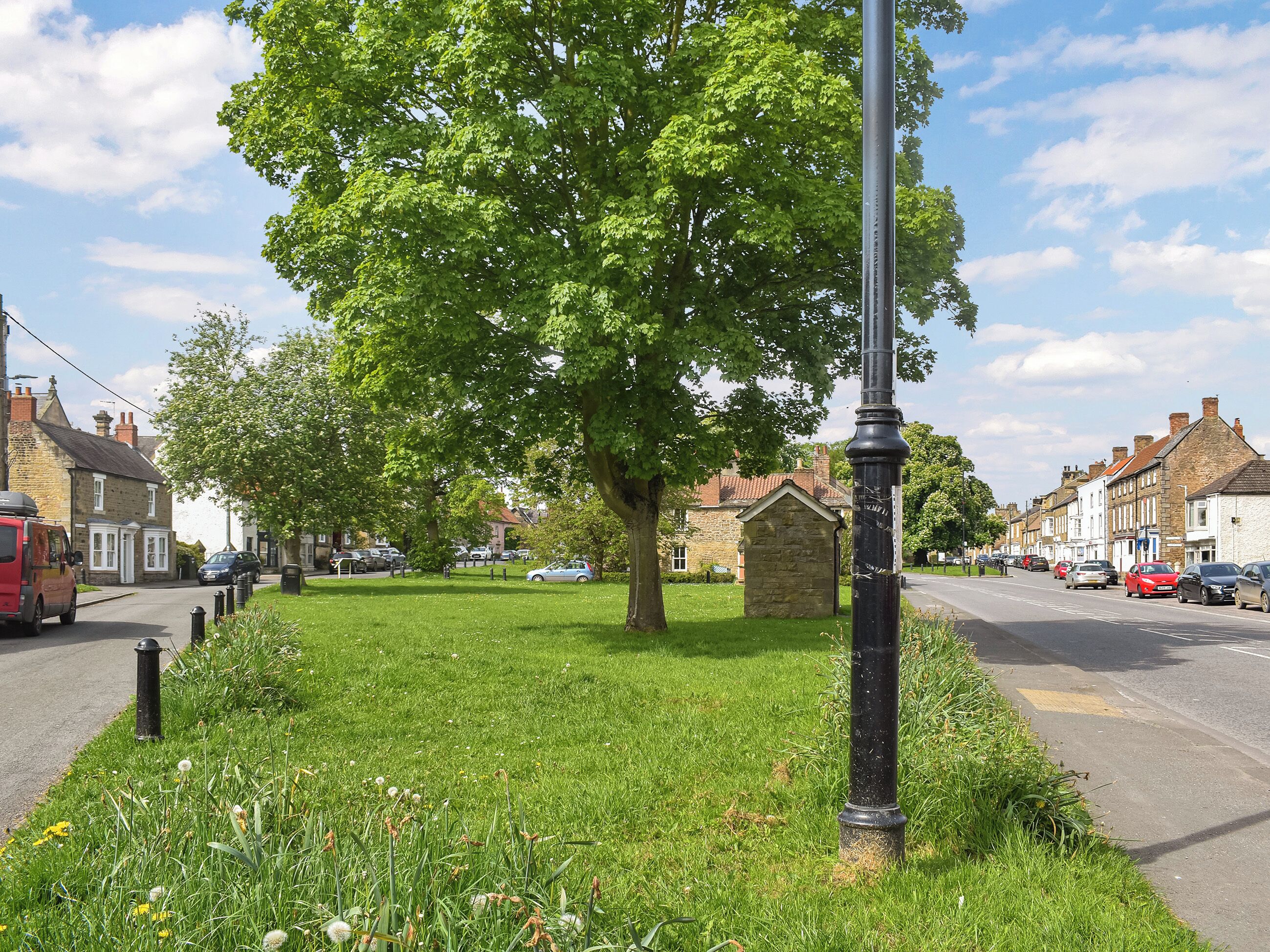 A street with a lamppost, a grassy area, and buildings.