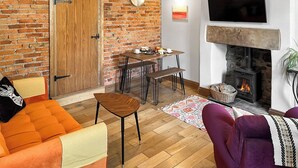 Een woonkamer met een bakstenen muur, een open haard, een tv die erboven bevestigd is, en een eethoek met een tafel en stoelen.