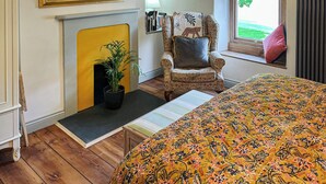 Een kamer met een bed, een stoel, een open haard, een raam met gordijnen en een spiegel aan de muur.